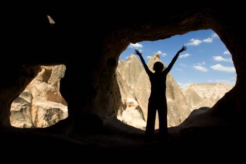 Silhouetted woman in door of primitive home built into rock.